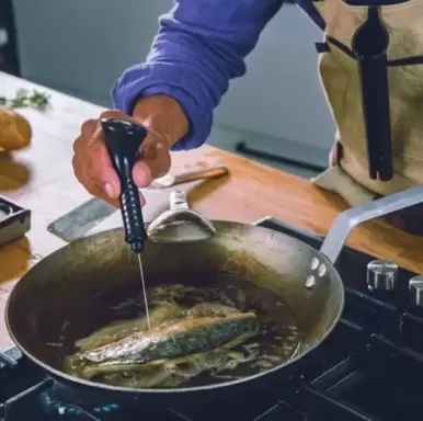 Kock som mäter temperatur på fisk i stekpanna