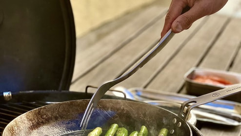 Matlagningsgaffel med sparris i stekpanna på grill